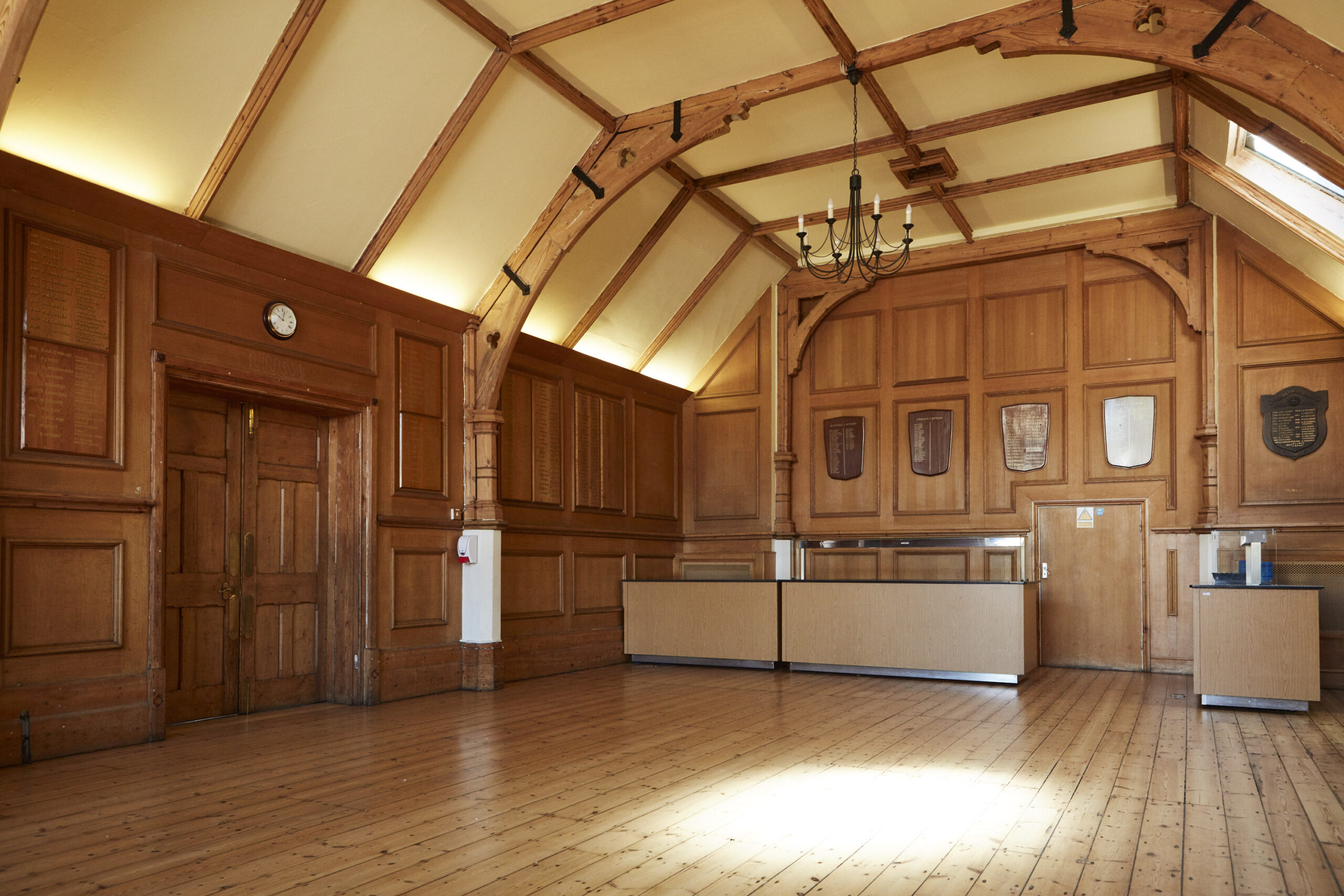 The inside of an empty school dining room. The floors and walls are wood, and there are shields on the walls.