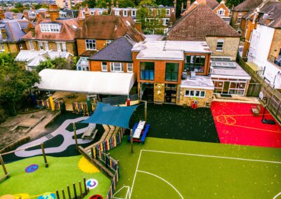 A drone photo of a school playground. The playground is in the foreground with the building at the back. Play equipment is visible in the playground.