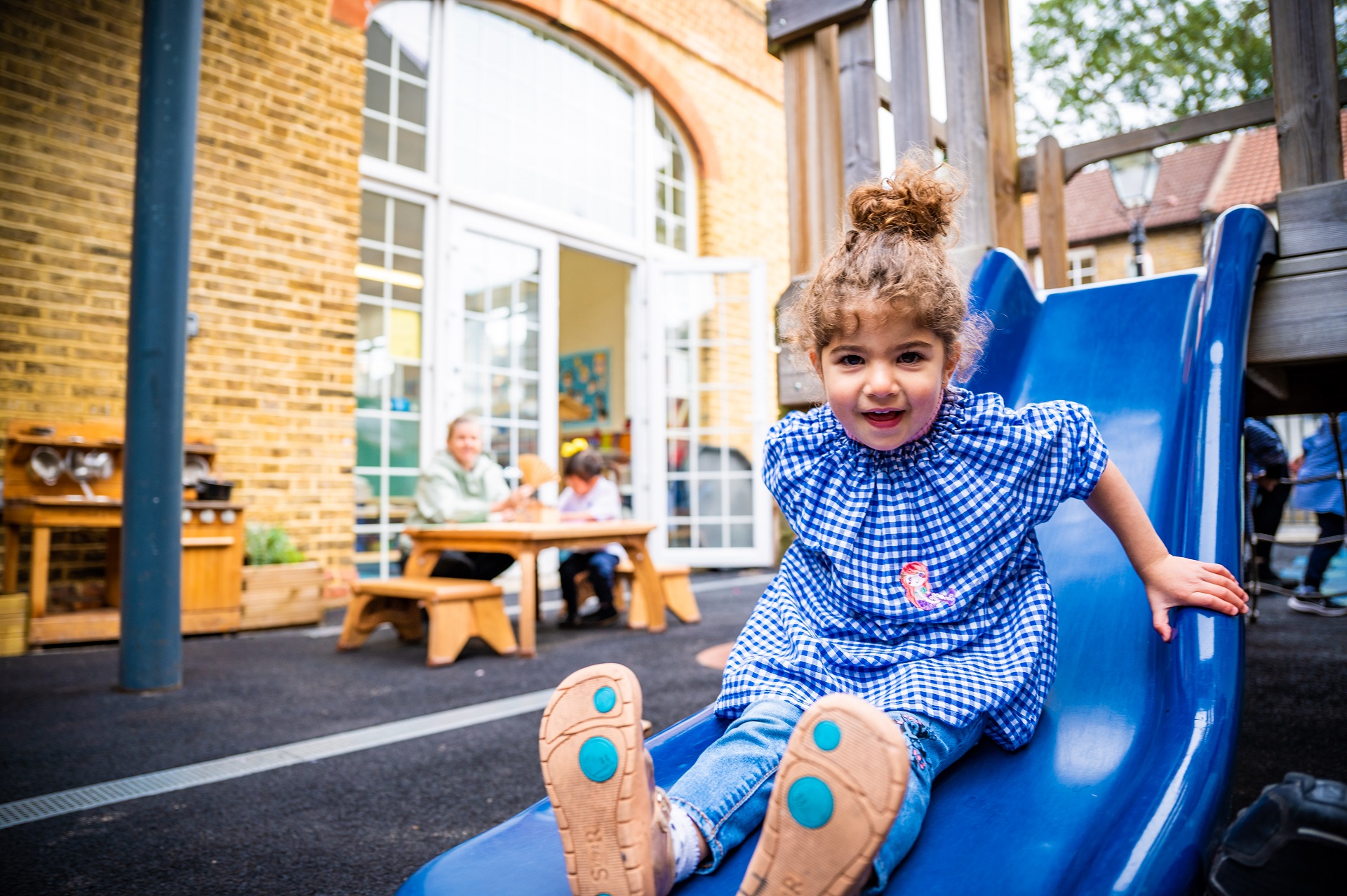A Nursery pupil slides down a blue slide in the playground.