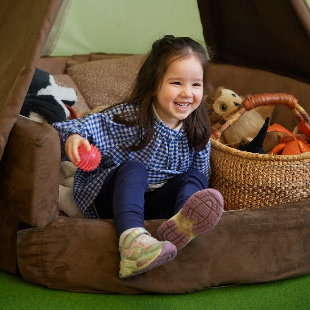 A Nursery pupil sits on cushions and throws a ball.