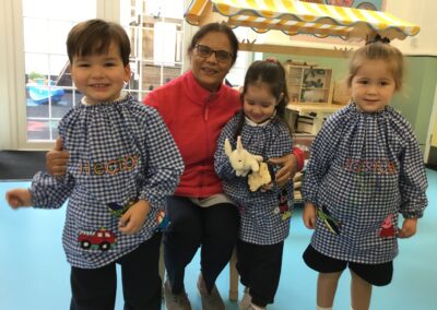 Three Nursery children stand with a KHS grandmother in the classroom.