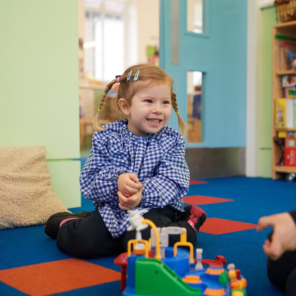 A Nursery pupil sits on the floor of Butterfly classroom playing with lego.